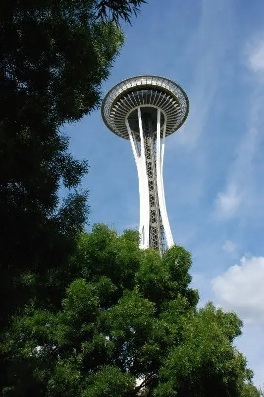 The Space Needle rising above trees against a blue sky with light clouds