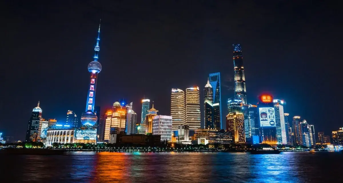 Shanghai's Oriental Pearl Tower and Lujiazui skyline lit up at night, seen across the Huangpu River