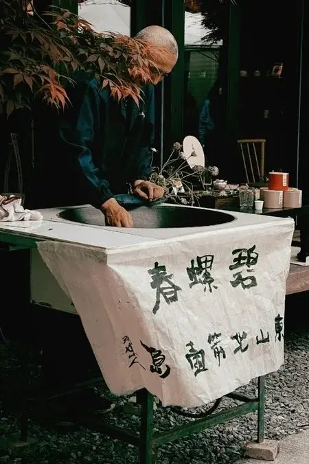 A tea master roasting Biluochun green tea leaves by hand at an outdoor stall in Suzhou