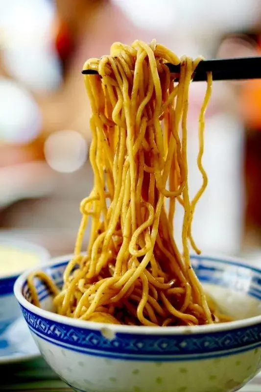 A bowl of Wuhan hot-dry noodles, sesame paste tossed through thick noodles, lifted with chopsticks