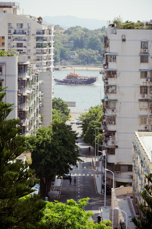 A Xiamen street view with apartment towers and a tour boat on the water in the background