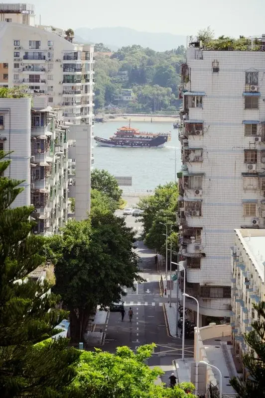 A Xiamen street view with apartment towers and a tour boat on the water in the background