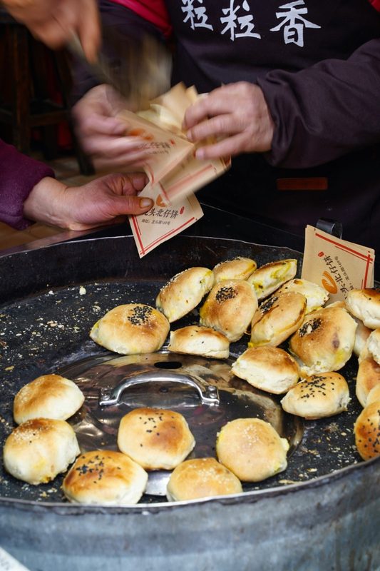 A street vendor selling fresh-baked sesame buns from a large metal tray in Xiamen