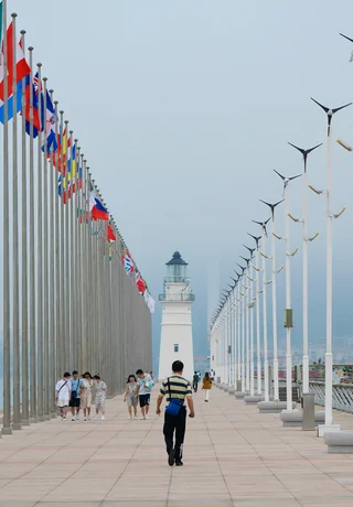 Visitors walking past the flag plaza and lighthouse on the Qingdao waterfront