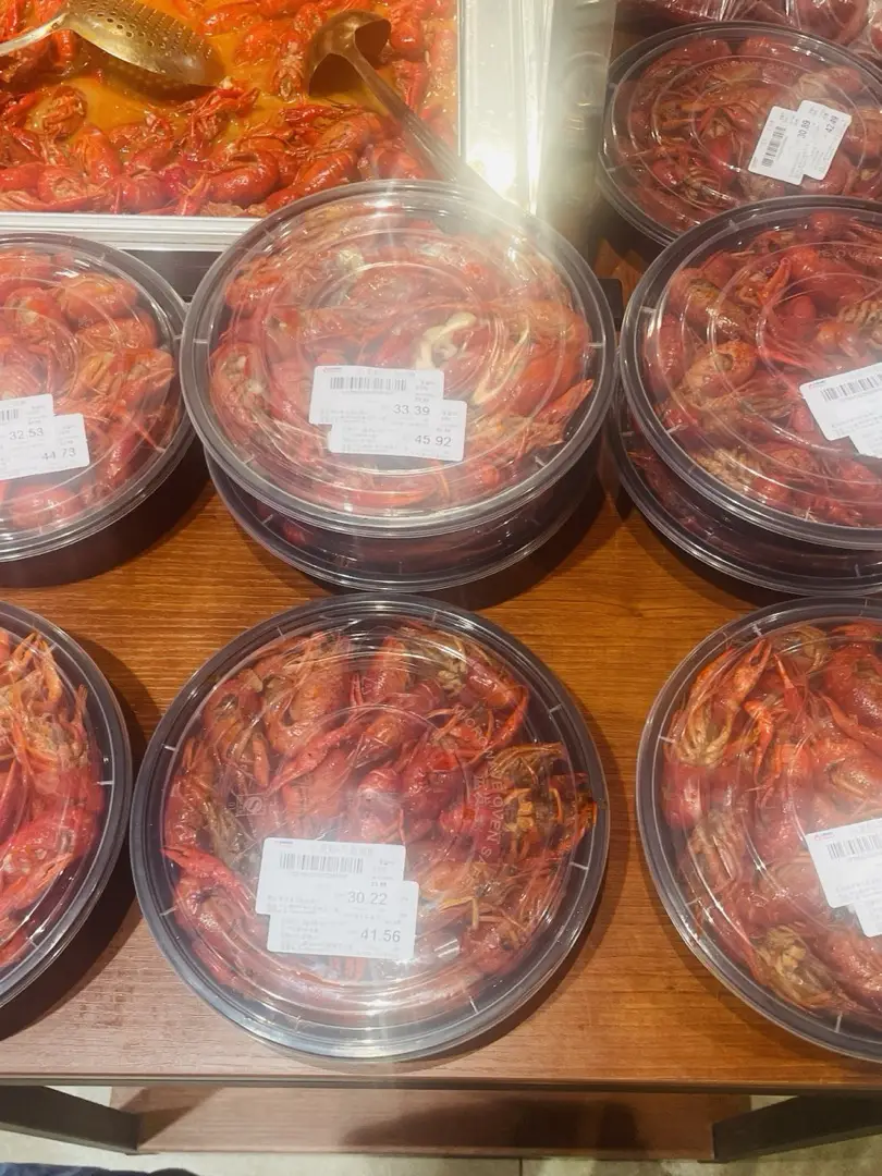 Supermarket ready-to-eat counter in China with packaged crayfish and braised dishes in plastic tubs, each tub carrying a printed price sticker