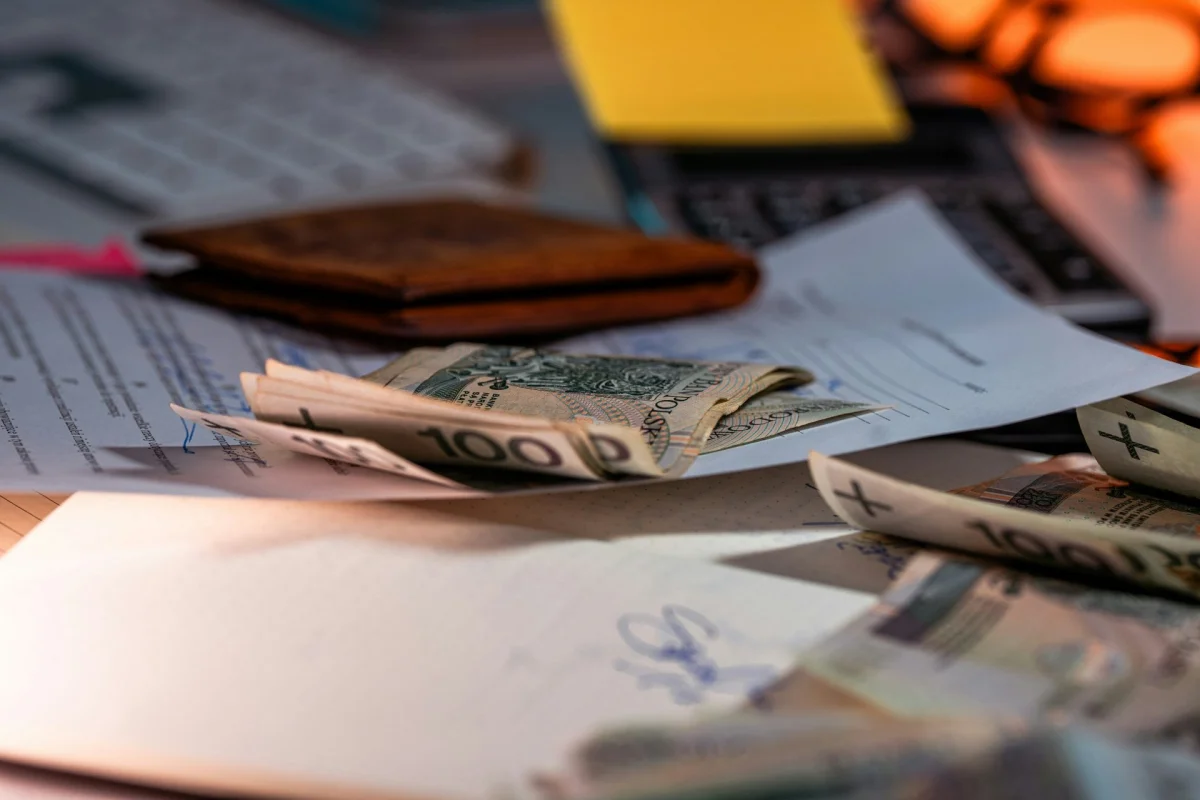 Cash, a wallet and paperwork spread across a desk under warm light