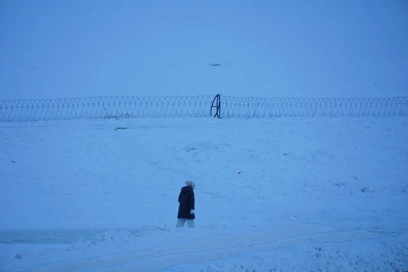 A person in dark winter clothing walks through deep snow in Mohe.