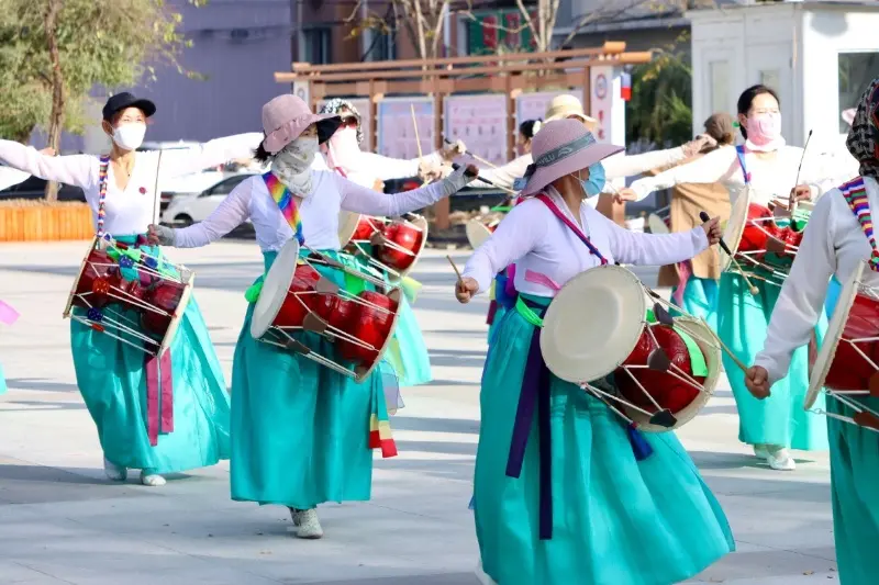 Women in traditional colorful Hanbok dresses performing a folk drum dance on a sunny day in Yanji, celebrating local culture