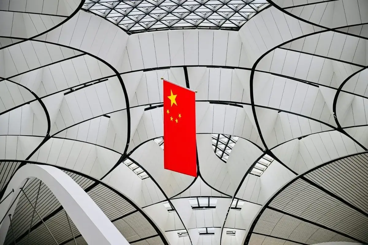 Upward view of Beijing Daxing International Airport's terminal ceiling, radiating steel ribs with a Chinese flag hanging in the center