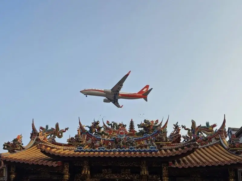 A jet on approach passing low over an ornate temple roof with dragon and phoenix ridge sculptures