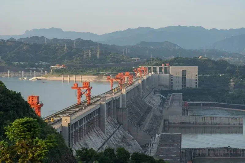A large hydroelectric dam with orange gantry cranes spanning a wide river valley