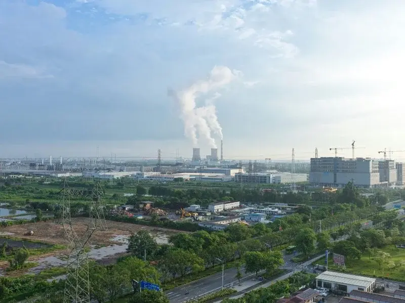 A thermal power plant with cooling towers releasing steam, seen across an industrial cityscape