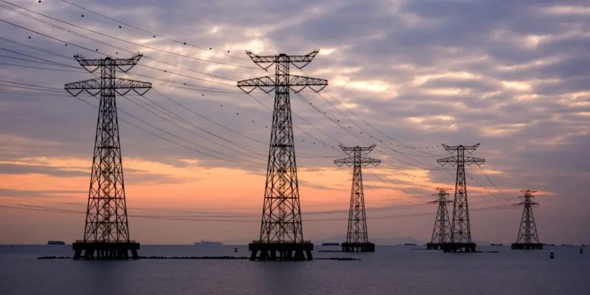 Transmission towers carrying power lines out over open water at sunset