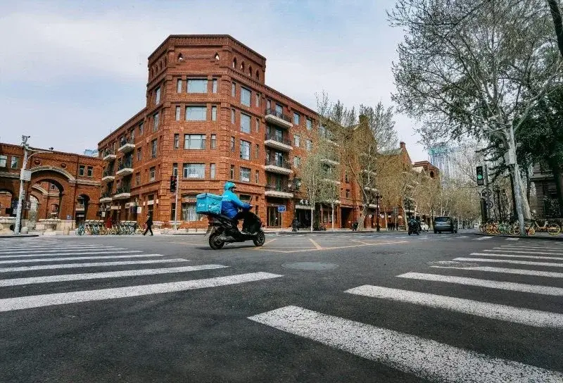 An Ele.me rider in a blue uniform riding through a street lined with red-brick colonial-era buildings