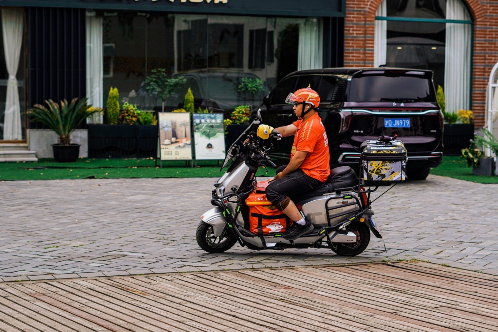 A JD delivery rider in an orange-red uniform parked on a wooden boardwalk