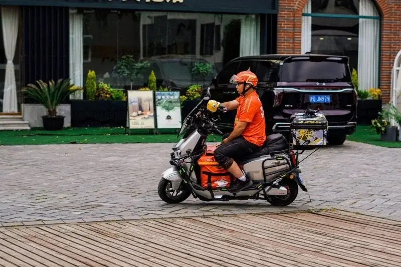 A JD delivery rider in an orange-red uniform parked on a wooden boardwalk