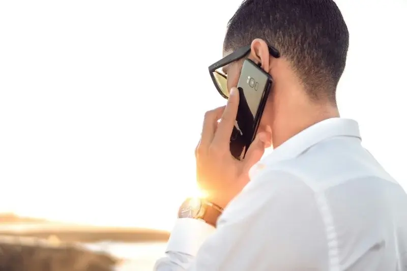 A person on a phone call outdoors at sunset, phone held to their ear