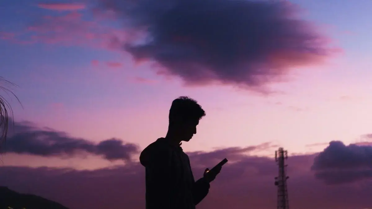 Silhouette of a person checking their phone at dusk, with a telecom signal tower visible in the background
