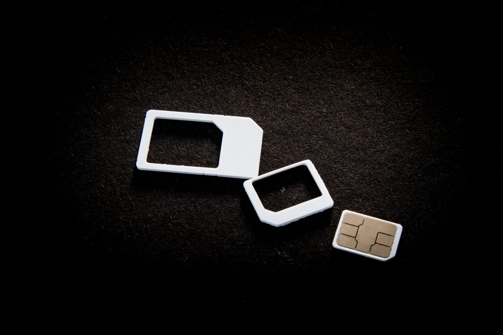 A disassembled SIM card adapter set on a dark background, showing the standard, micro, and nano SIM sizes