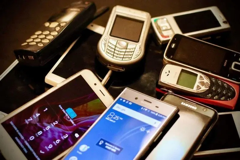 A pile of old mobile phones from different eras, from basic keypad models to early smartphones
