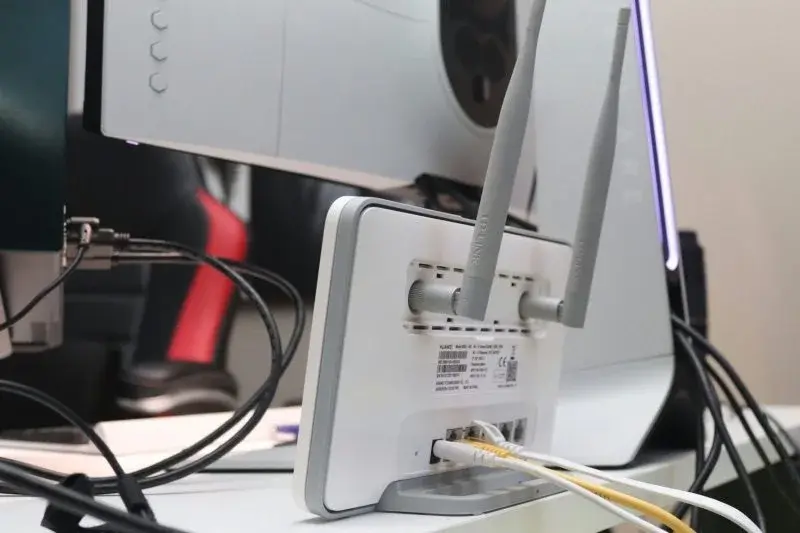 The back of a home Wi-Fi router with antennas raised, connected via ethernet cables to a fiber modem