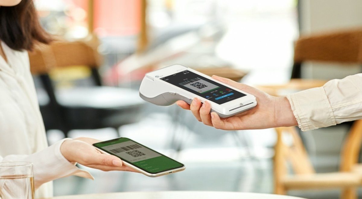 Close crop of a payment terminal displaying a QR code alongside a customer's phone showing a scan-to-pay screen