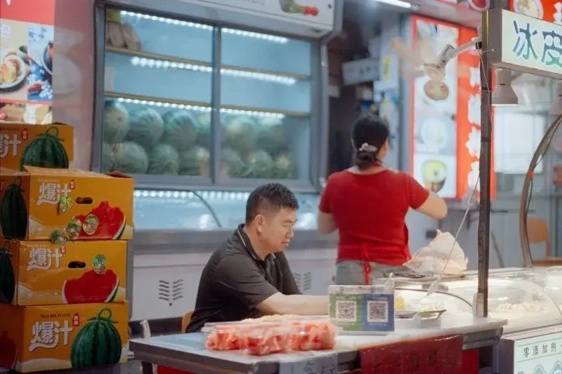 A fruit stall with a printed QR payment code displayed at the counter