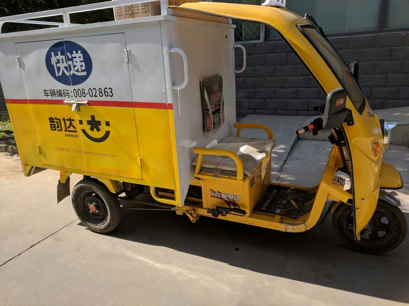 A yellow Yunda Express delivery tricycle parked on a sidewalk