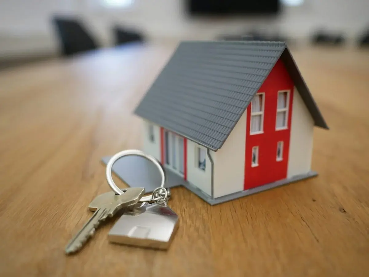 A small house-shaped keychain with a set of keys resting on a wooden table