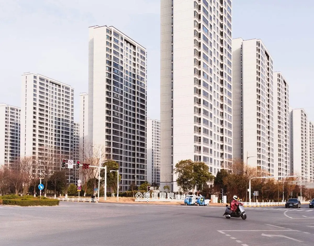A row of newer high-rise apartment towers in Nanjing at a wide intersection, with an electric scooter crossing in the foreground