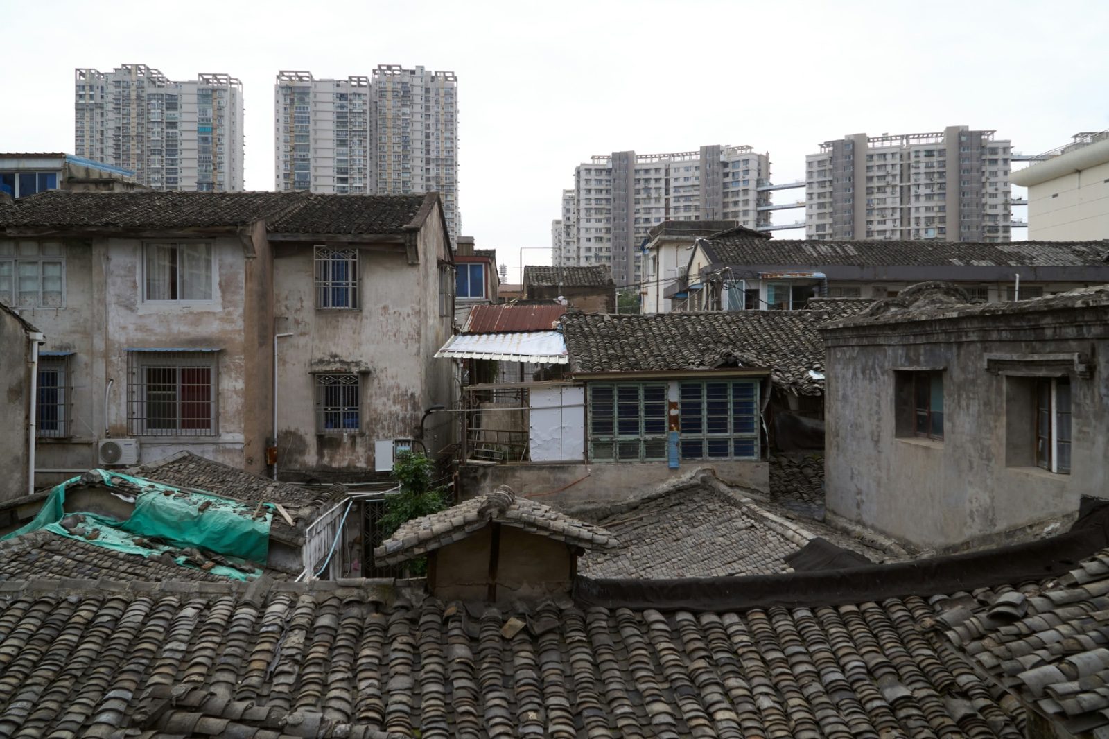 Old tiled-roof residential buildings in the foreground in Wenzhou, with modern high-rise apartment towers rising directly behind them