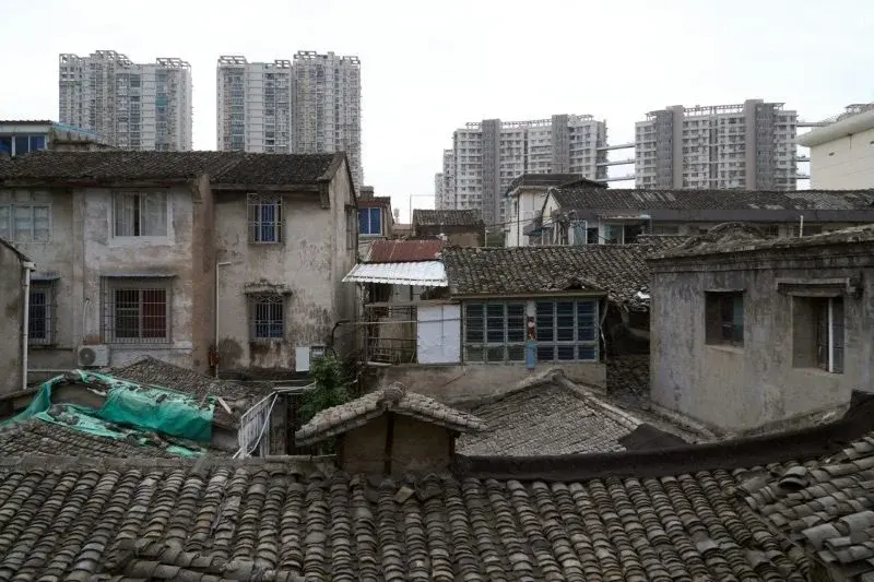 Old tiled-roof residential buildings in the foreground in Wenzhou, with modern high-rise apartment towers rising directly behind them