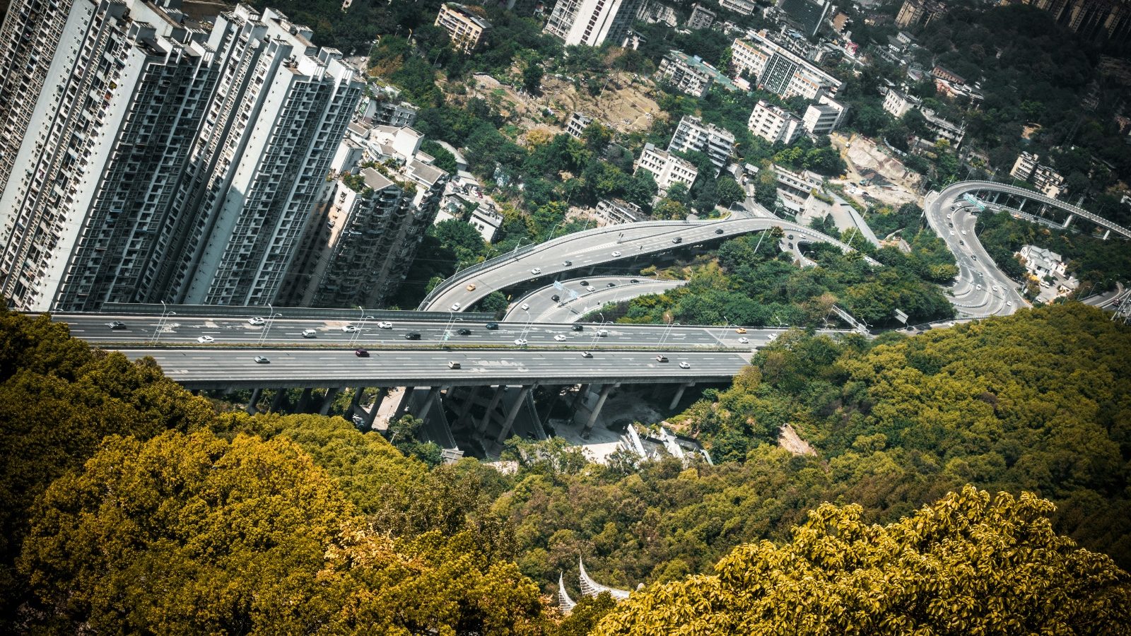 Aerial view of a multi-level elevated highway winding through hilly, forested terrain in Chongqing