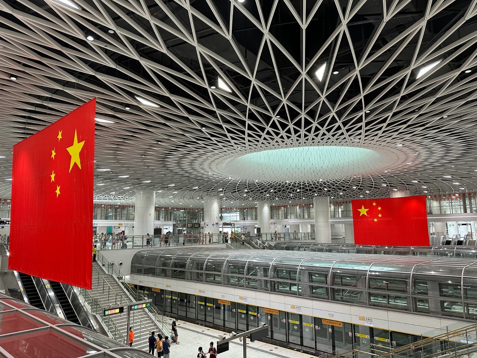 Large concourse of a modern metro station with large Chinese national flags hanging from the ceiling