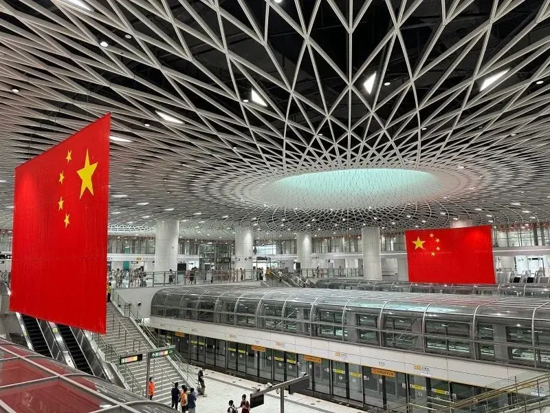 Large concourse of a modern metro station with large Chinese national flags hanging from the ceiling