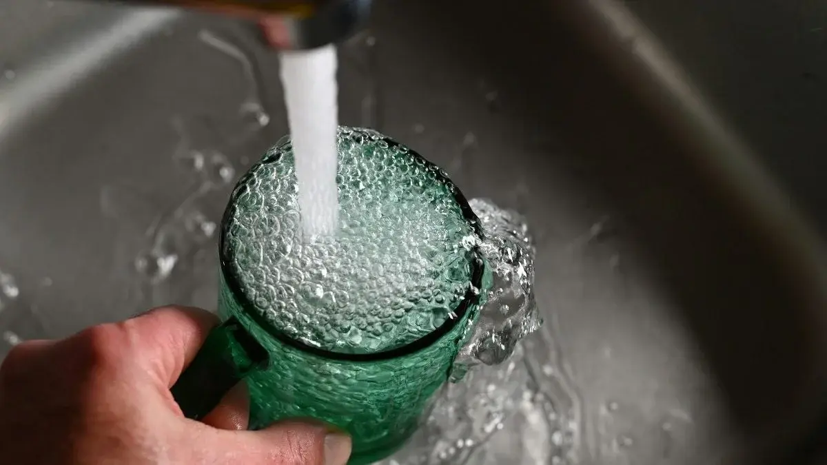 Tap water pouring into a green glass mug at a kitchen sink