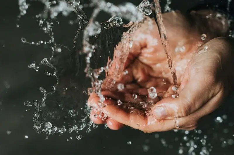 Water splashing dramatically into cupped hands against a dark background