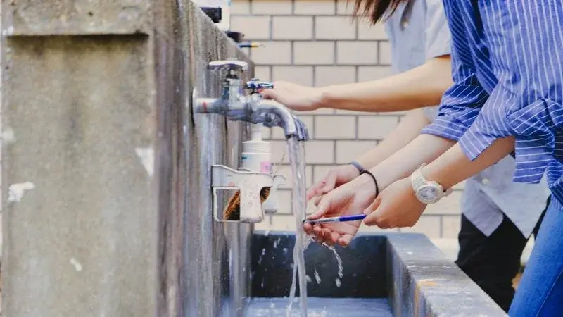 Two people washing their hands at an outdoor tap and basin
